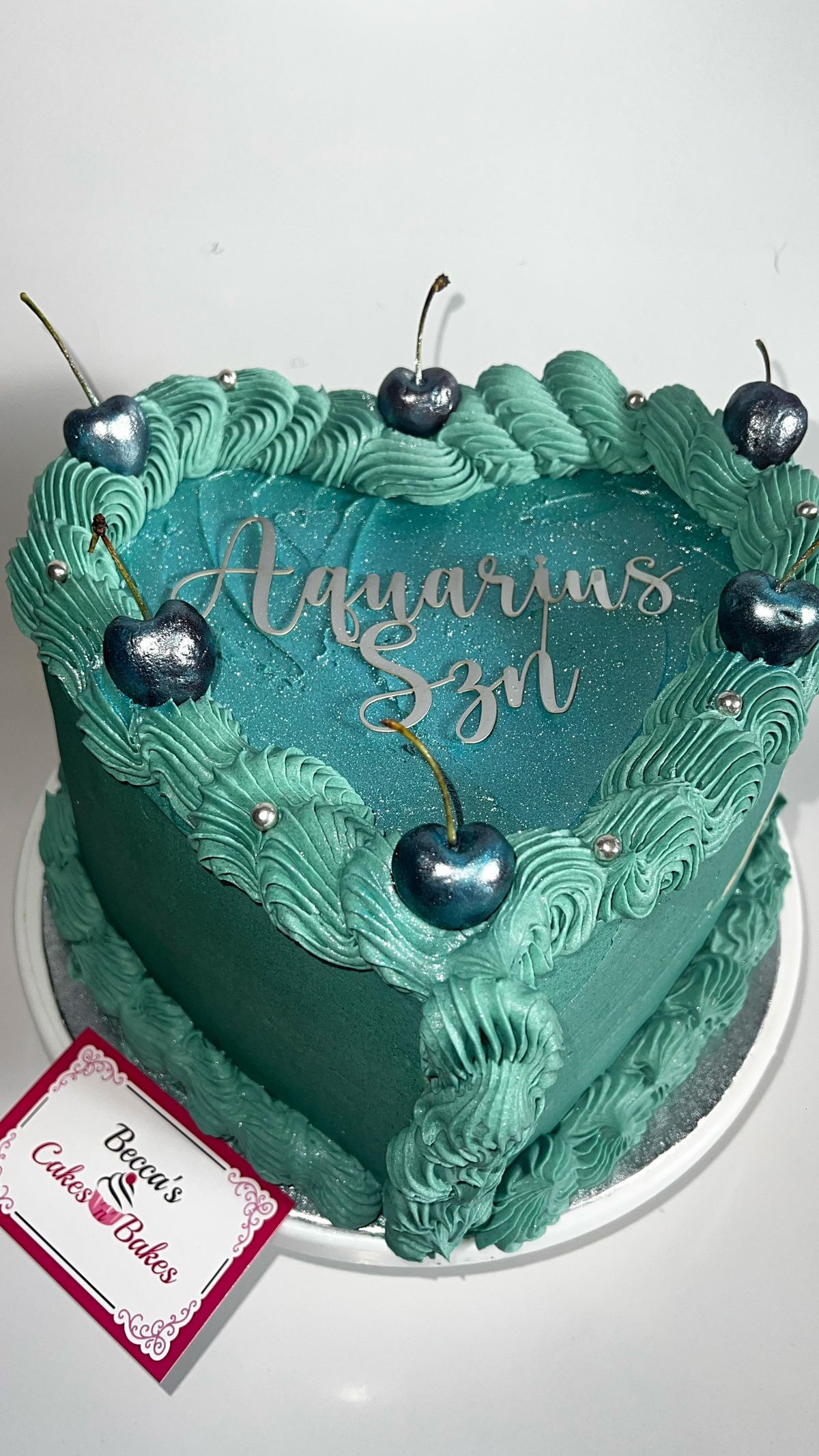 A green heart-shaped cake with cherries and gold lettering
